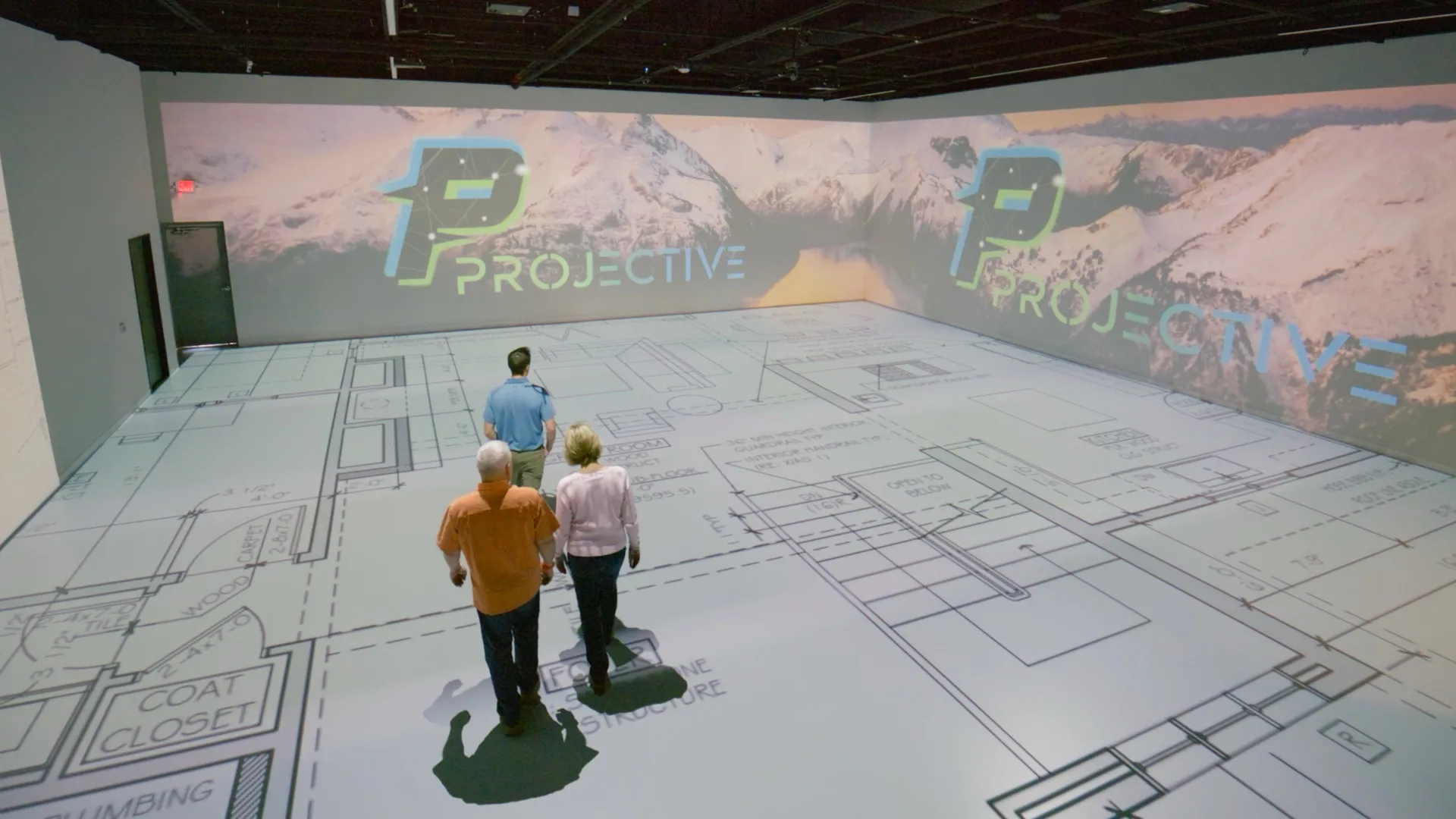 Projective Studios — clients exploring 1:1 floor plan with Projective branding on walls